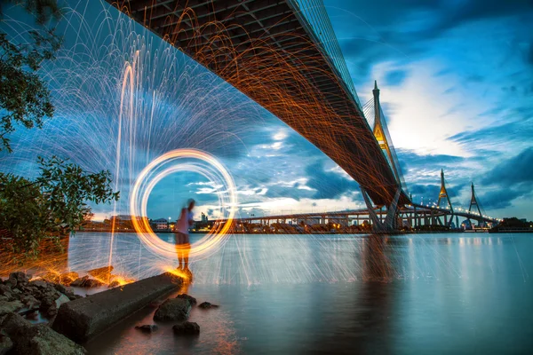 Hot Golden Sparks Flying from Man Spinning Burning Steel Wool under Bhumibol Bridge in Bangkok Thailand., Long Exposure Photography using Steel Wool Burning.