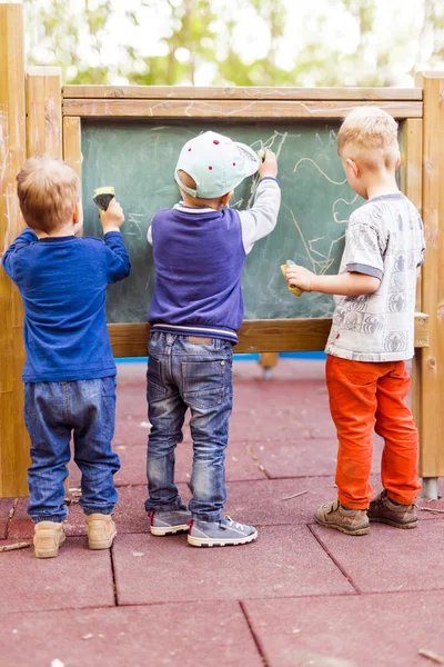 Three boys drawing on a blackboard