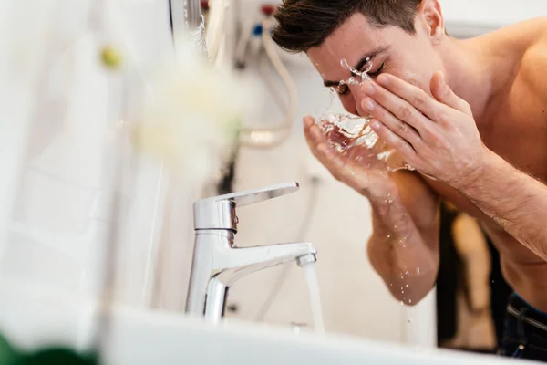 Handsome man washing face in bathroom