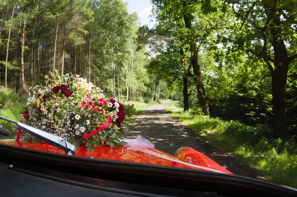 Bouquet of roses, daisies and other wild flowers as wedding decoration on a red vintage car