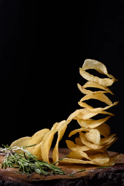 Stack of potato chips with herbs, tasty snack on wood, closeup.