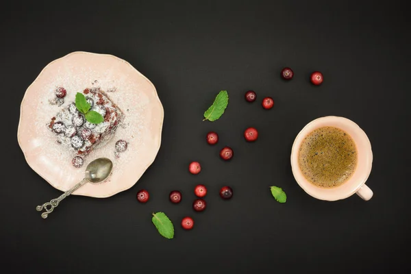 Chocolate dessert, cup of coffee and fresh cranberry over black background. Top view.