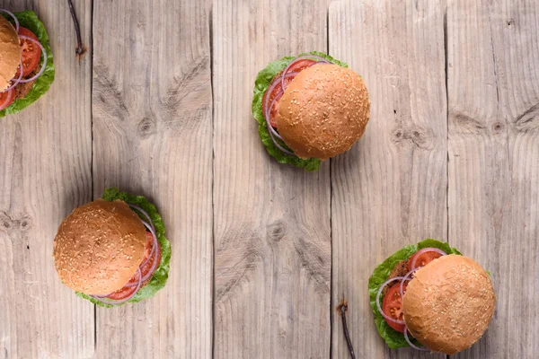Fresh homemade burgers over rustic wooden table, top view, copy space.