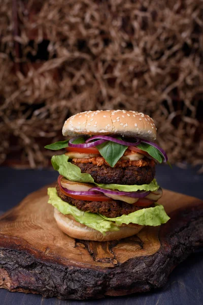 Double burger  with succulent beef patty and fresh vegetable ingredients served on a rough wood board.