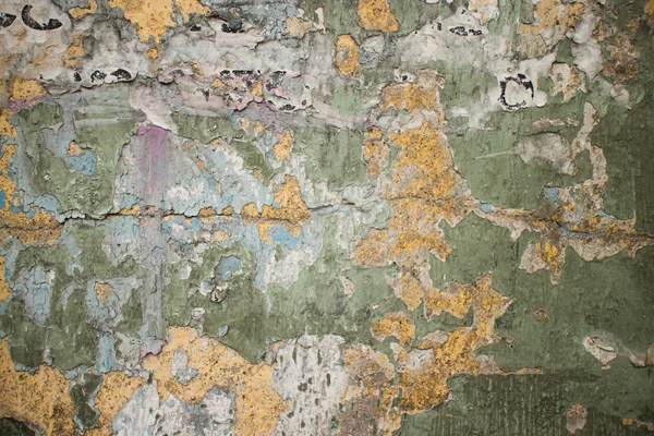 Old cracked wall in Thailand with flecks of paper and chipped green and beige paint remants