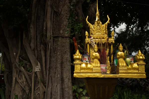 Horizontal close up of a gold spirit house and large tree in Sou