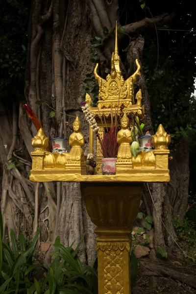 Medium close up of a gold spirit house and large tree in Southeast Asia
