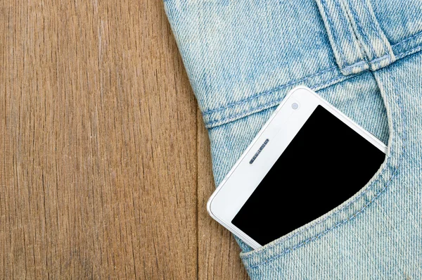 White smart phone in jeans pocket on wooden background.