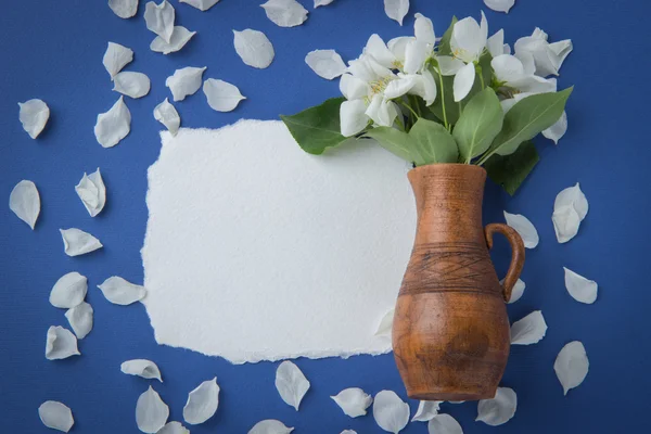 Greeting card with branches of apple blossom in a jug on a blue