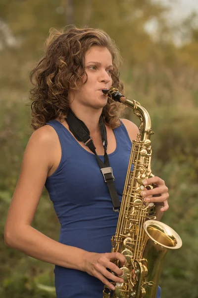 Beautiful girl in a blue t-shirt playing the saxophone in gold o