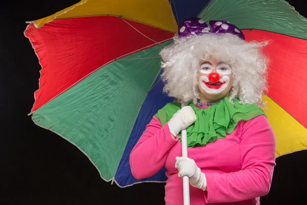 Jolly good funny clown with a multi-colored umbrella on a black