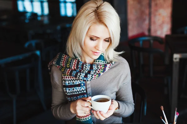 Blonde girl sitting in cafe with cup of tea