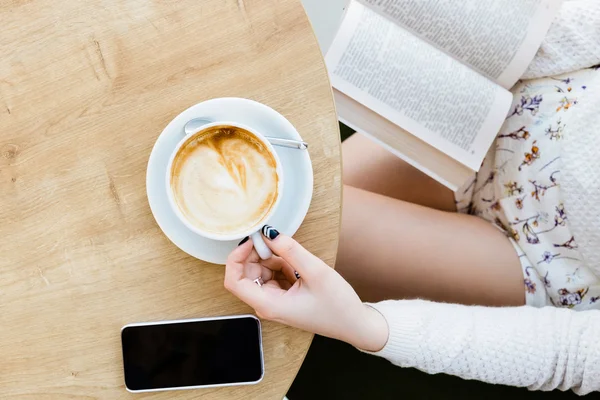 Girl's legs, cup of coffee, book and mobile phone