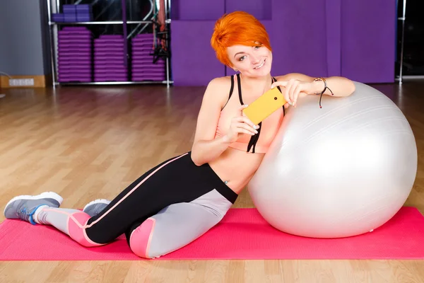 Redhead woman with phone in gym