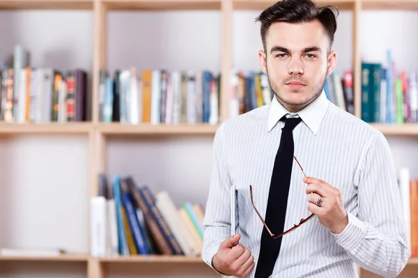 Businessman standing with glasses on the bookshelves background