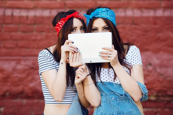 Brunette twins girls hiding behind tablet