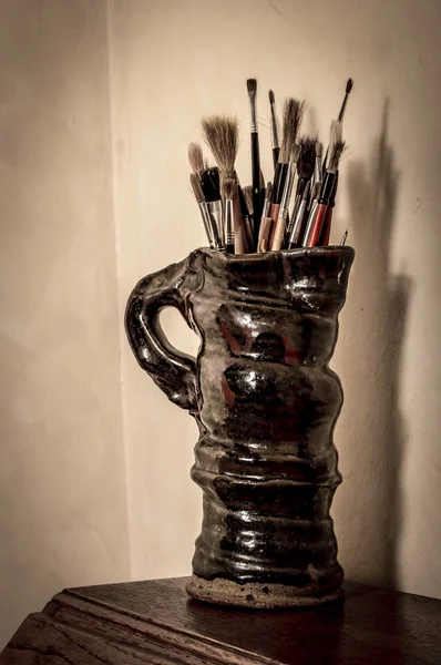 Artists paint brushes in pottery jug. Vintage filter effects applied.