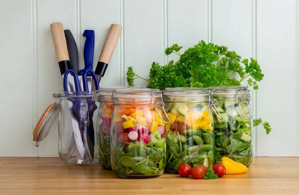 Salad in glass storage jars on kitchen worktop.