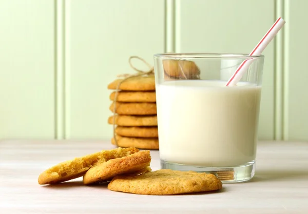 Refreshing glass of milk with a drinking straw, and delicious snack of homemade peanut butter cookies. With a tied stck of cookies in the background.