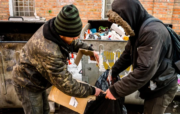POLTAVA, UKRAINE - 18 FEBRUARY 2016: Two young men near the garbage can collecting paper for recycling. Inflation in the country has reduced the cost of money three times.