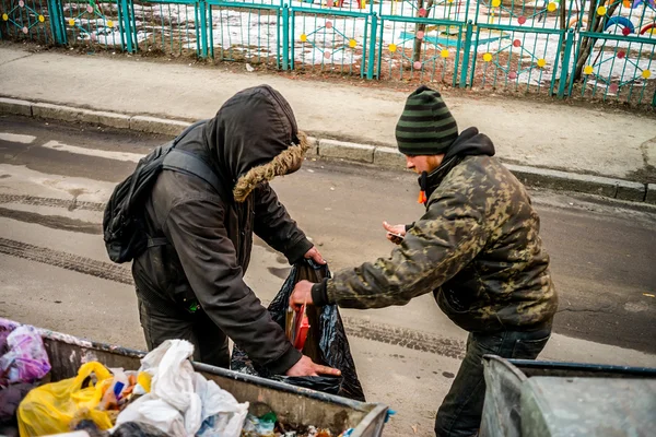 POLTAVA, UKRAINE - 18 FEBRUARY 2016: Two young men near the garbage can collecting paper for recycling. Inflation in the country has reduced the cost of money three times.