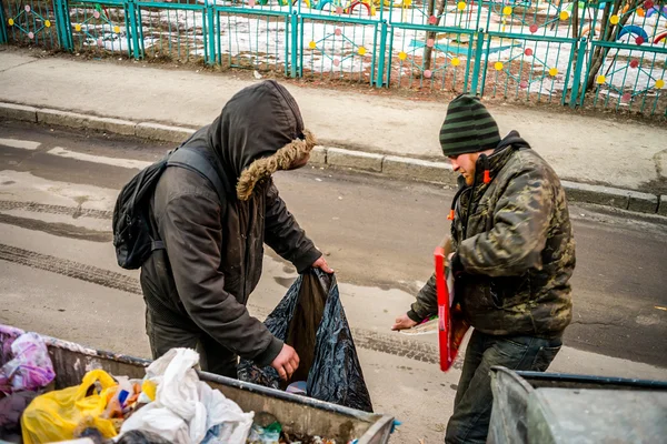 POLTAVA, UKRAINE - 18 FEBRUARY 2016: Two young men near the garbage can collecting paper for recycling. Inflation in the country has reduced the cost of money three times.