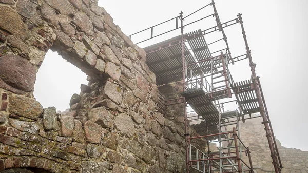 Ruined medieval castle wall with scaffolding and window in fog.