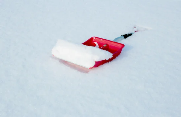 Red shovel for snow removal lying in the snow