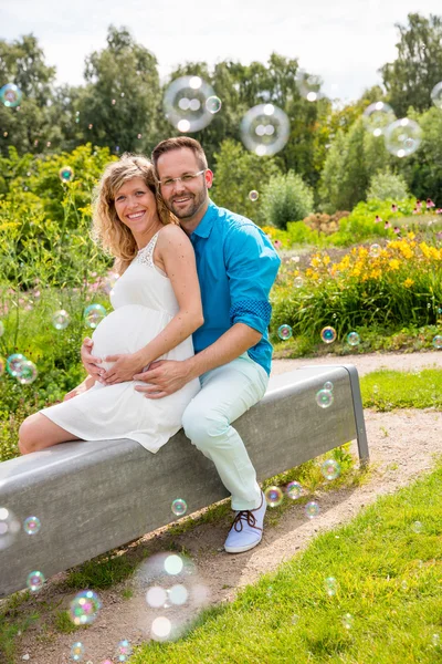 Happy couple expecting baby, sitting on bench in park