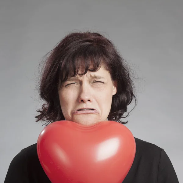 Sad brunette woman with heart shaped balloon against gray background