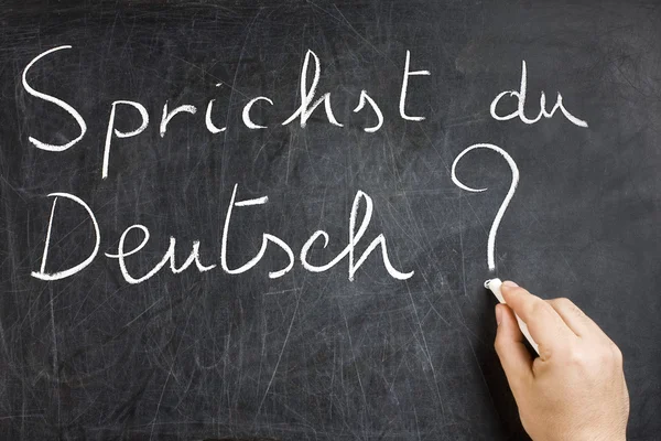 Do you speak German question handwritten on dirty chalkboard by male hand holding white chalk