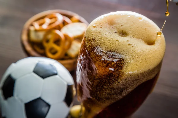 Pouring beer into glass with snacks and football