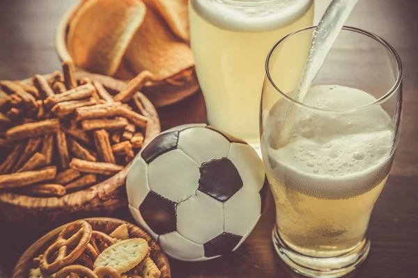 Pouring beer into glass with snacks and football