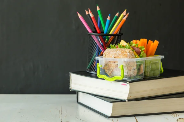 School lunch box with books and pencils in front of black board