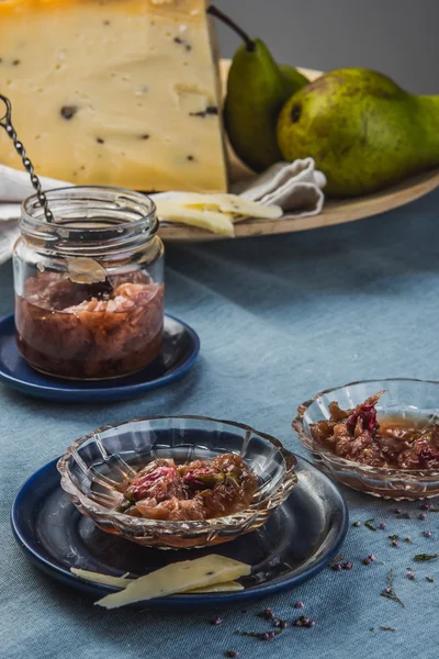 Small jam dishes with rose petal jam, pears and a big piece of cheese on a turquoise table-cloth.