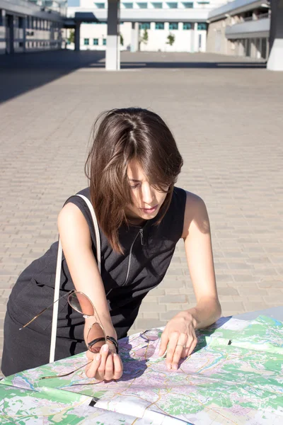 Attractive foreign female model looking on printed paper map in search of fastest directions to nearest hotel, restaurant, shopping center, main city square