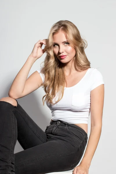 Awesome caucasian attractive sexy professional female model with blond hair posing in studio wearing white shirt and black ragged jeans, isolated on white background