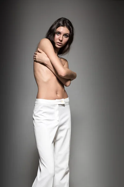 Portrait of young European beautiful sexy brunette fashion model in pants, awesome makeup, natural look, long hair, blue eyes, full lips, perfect skin is posing topless in studio for glamour vogue photo shoot