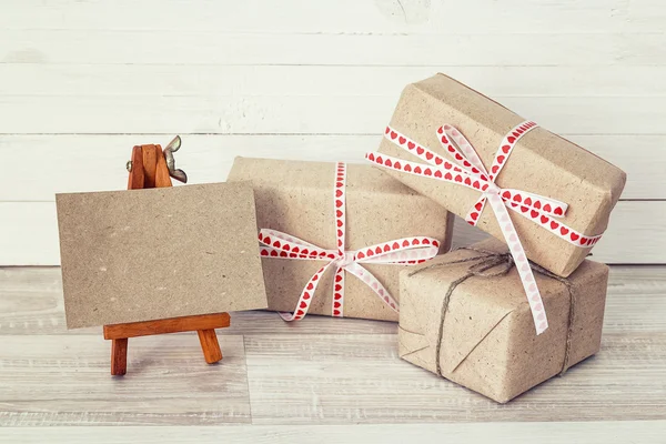 Gift boxes with miniature easel and blank card on white wooden b