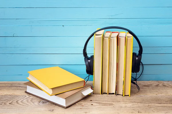 Audio book concept, book and headphones over wooden background.