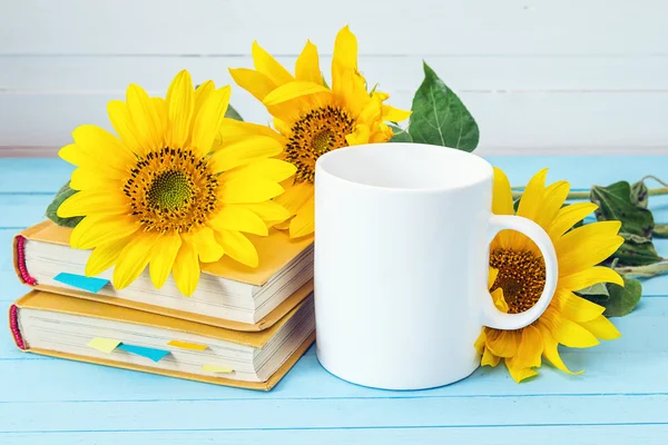 White coffee cup with sunflowers and yellow books on blue wooden