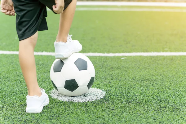 Feet of a boy wearing white sneakers stepping on a soccer ball.