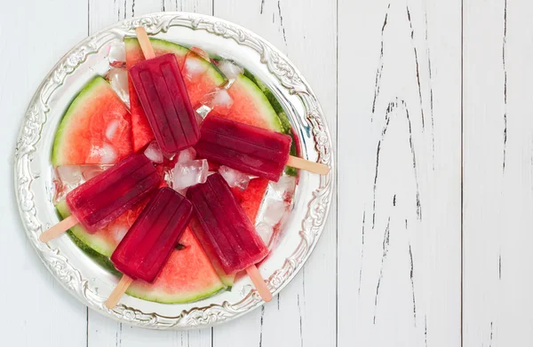 Watermelon popsicles - ice pops - on slices of ripe juicy organic watermelon, served on vintage silver tray over old rustic wooden background. Copy space