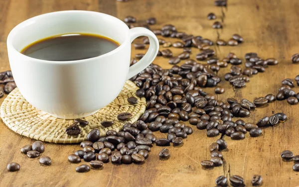 A cup of coffee and coffee beans on wood background, warm toning