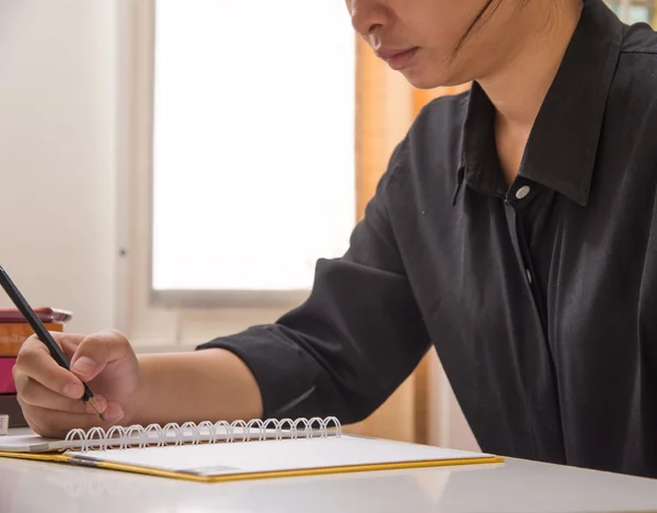 A young woman is sitting at a table and is writing in a notebook