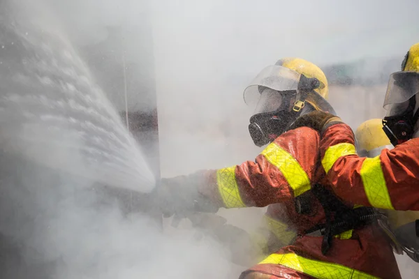 Two firemen in fire fighting suit spraying water to fire surroun