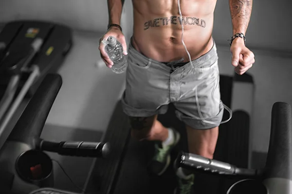 Sexy torso of wet man fall off treadmill or running track in gym drinking water.