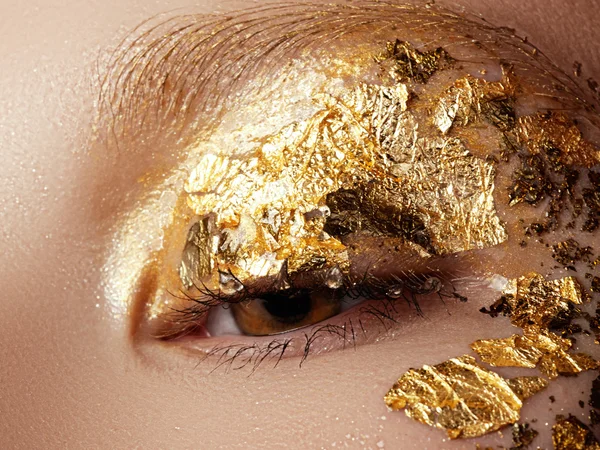 Cosmetics and make-up. Closeup macro shot of fashion sparcle visage. Closeup portrait of beautiful young woman with golden foil on face. Creative makeup