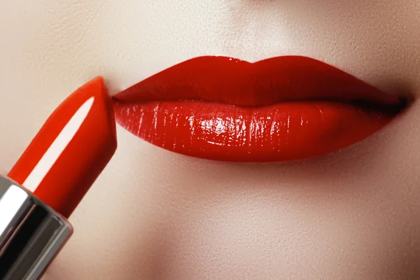 Extreme close up on model applying red lipstick. Makeup. Professional fashion retro make-up. Red lipstick