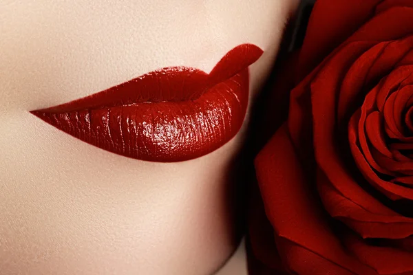 Close-up shot of sexy woman lips with dark red lipstick and beautiful red ros